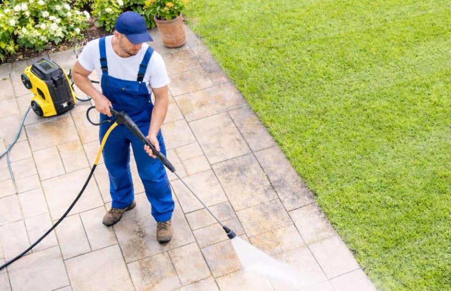 Mann reinigt mit Hochdruckreiniger eine Terrasse in einem Garten.