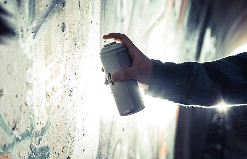 Eine Hand sprüht Graffiti an eine Wand mit lebendigen Farben.