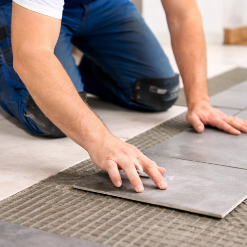Ein Handwerker verlegt Fliesen auf einem vorbereiteten Untergrund.