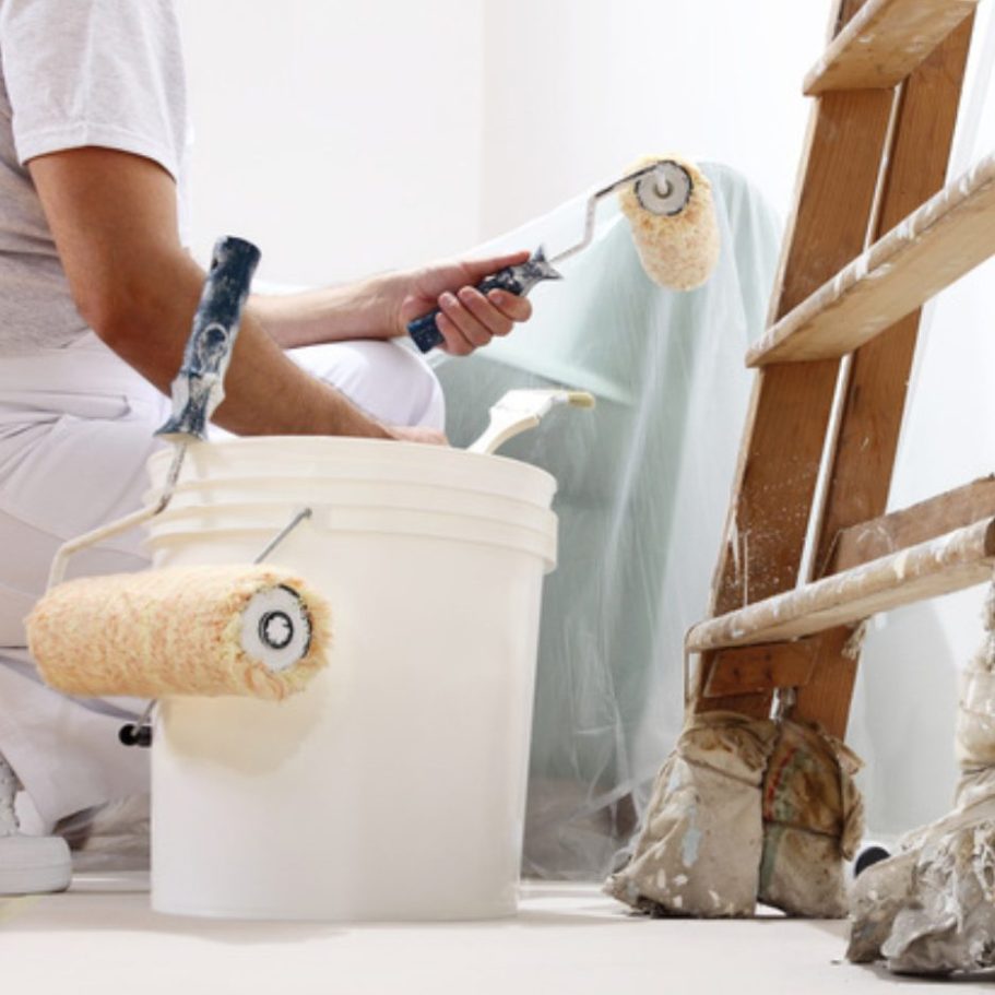 Ein Maler arbeitet mit einer Farbrolle und einem Eimer Farbe neben einer Leiter.